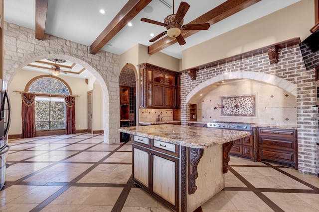 kitchen featuring light stone counters, ceiling fan, a kitchen island, and beam ceiling