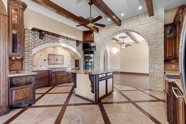 kitchen with a kitchen island, appliances with stainless steel finishes, a kitchen bar, beam ceiling, and light stone countertops