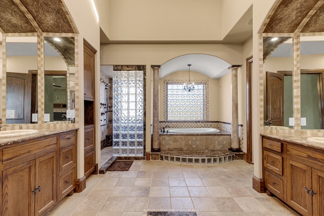 bathroom featuring a notable chandelier, a relaxing tiled tub, vanity, and decorative columns