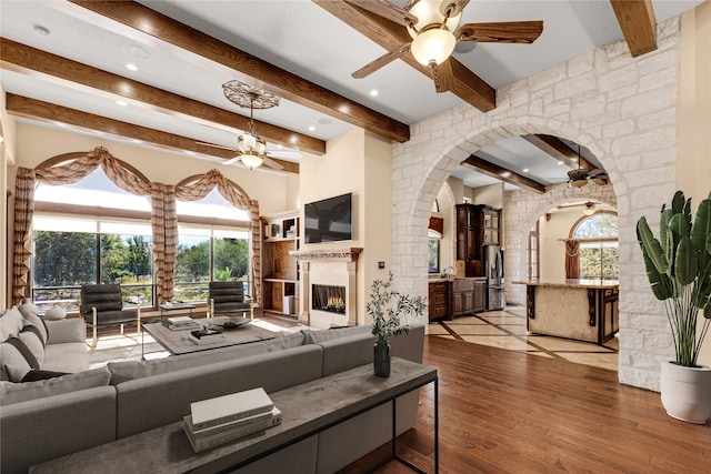 living room with beamed ceiling, a wealth of natural light, a large fireplace, and light hardwood / wood-style flooring