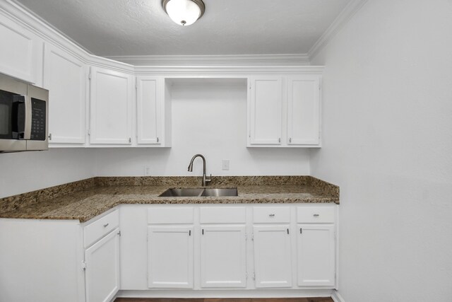 kitchen featuring dark stone counters, sink, ornamental molding, and white cabinets