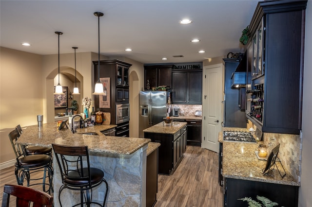 kitchen with wood-type flooring, stainless steel appliances, backsplash, hanging light fixtures, and kitchen peninsula