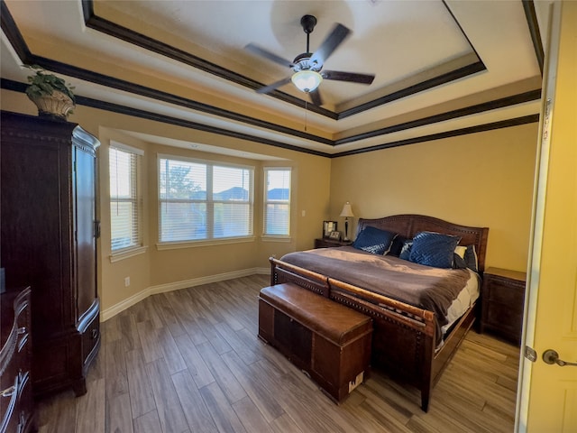 bedroom with ornamental molding, wood-type flooring, ceiling fan, and a tray ceiling