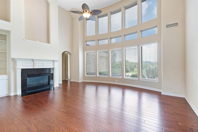 unfurnished living room featuring ceiling fan, a tile fireplace, dark wood-style flooring, baseboards, and built in features