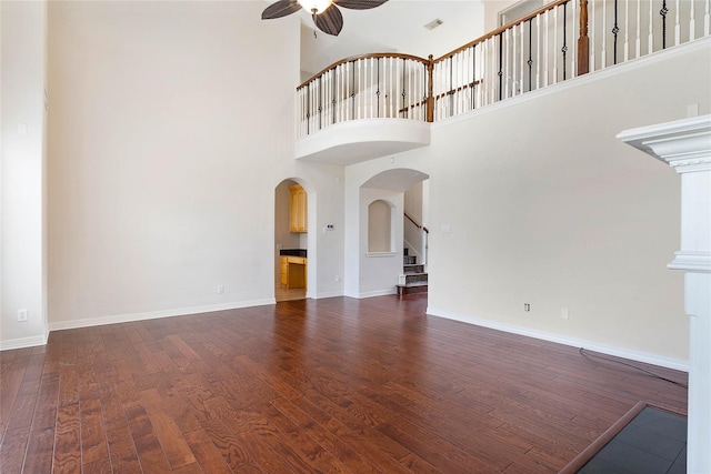 unfurnished living room with ceiling fan, dark wood-type flooring, and a high ceiling