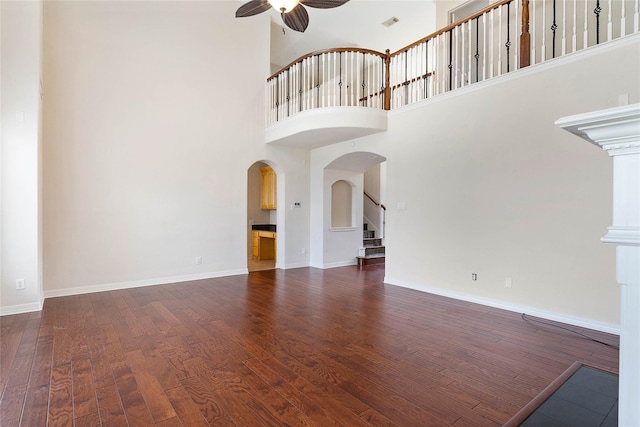 unfurnished living room featuring arched walkways, stairway, a ceiling fan, wood finished floors, and baseboards