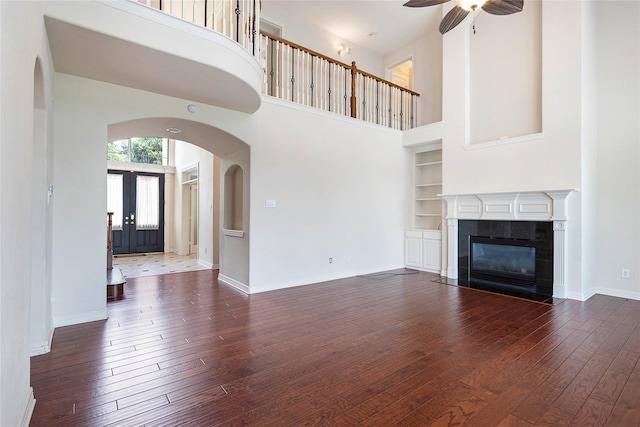 unfurnished living room with arched walkways, built in shelves, hardwood / wood-style flooring, a fireplace, and baseboards