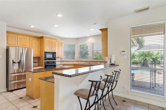 kitchen with a kitchen breakfast bar, kitchen peninsula, dark stone countertops, light tile patterned flooring, and black appliances