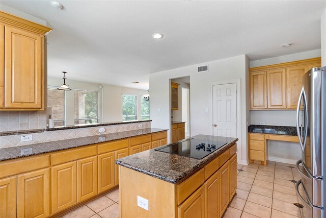 kitchen with stainless steel fridge, a kitchen island, black electric cooktop, and dark stone counters