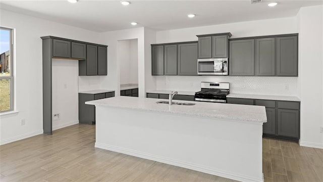 kitchen with a center island with sink, appliances with stainless steel finishes, sink, and gray cabinetry