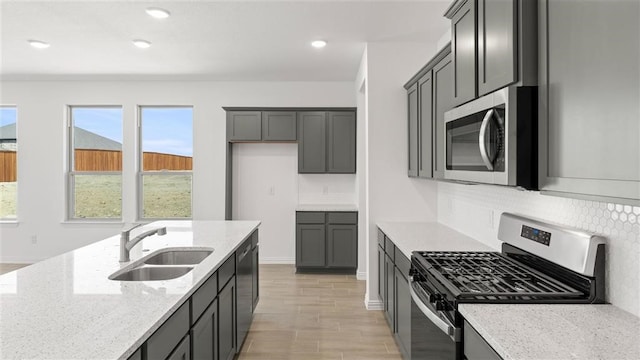 kitchen featuring light stone counters, light hardwood / wood-style flooring, sink, backsplash, and appliances with stainless steel finishes