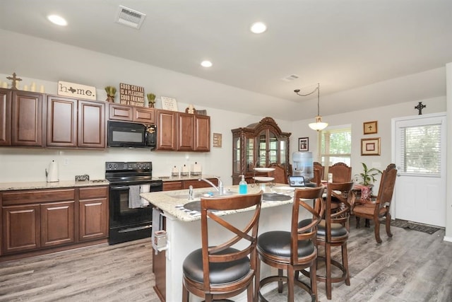 kitchen with a center island with sink, sink, black appliances, light wood-type flooring, and pendant lighting