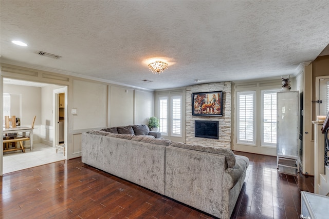 living room with a stone fireplace, a healthy amount of sunlight, a textured ceiling, and dark hardwood / wood-style flooring