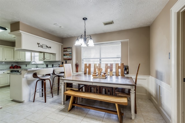 tiled dining room with a textured ceiling, a healthy amount of sunlight, and a chandelier