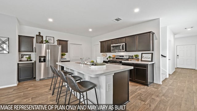 kitchen featuring stainless steel appliances, dark brown cabinetry, sink, an island with sink, and light wood-type flooring