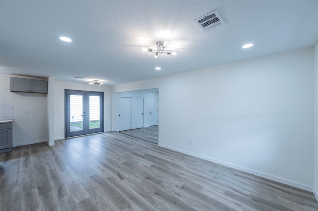 unfurnished living room with a chandelier, french doors, light wood-type flooring, and a textured ceiling