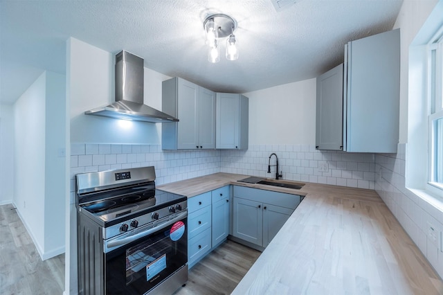 kitchen featuring sink, wall chimney exhaust hood, wood counters, stainless steel range oven, and backsplash