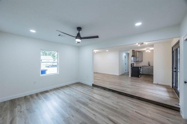 unfurnished living room with ceiling fan, light wood-type flooring, and sink