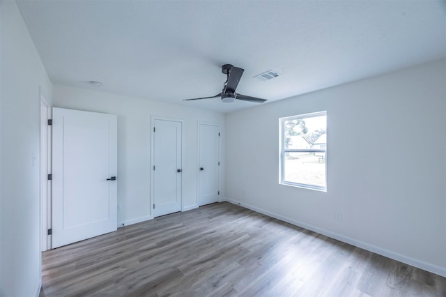 unfurnished bedroom with ceiling fan, wood-type flooring, and two closets