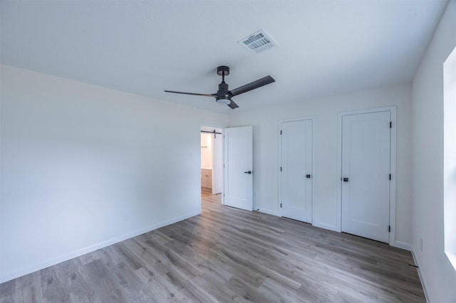 unfurnished bedroom featuring multiple closets, ceiling fan, and light hardwood / wood-style floors