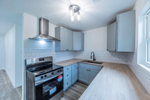 kitchen featuring gray cabinets, stainless steel electric range, butcher block counters, sink, and wall chimney exhaust hood