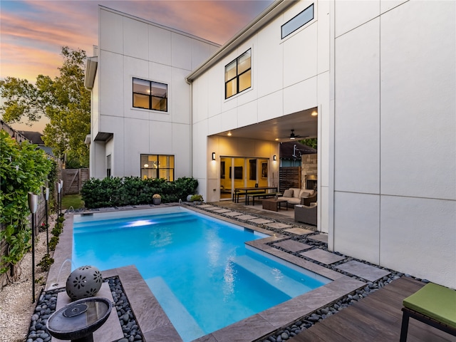 pool at dusk featuring ceiling fan, outdoor lounge area, and a patio