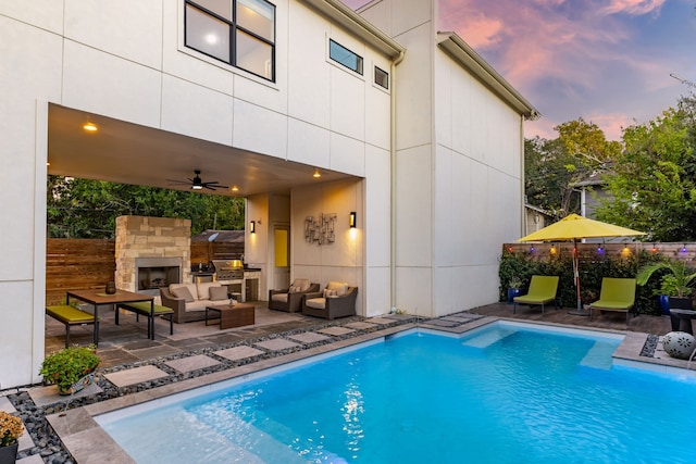 pool at dusk featuring an outdoor living space with a fireplace, ceiling fan, and a patio area