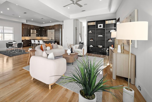 living room with ceiling fan, a raised ceiling, and light hardwood / wood-style flooring