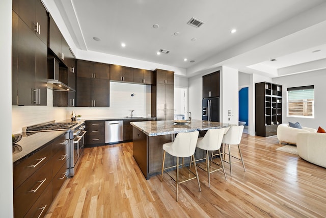 kitchen featuring a breakfast bar area, a kitchen island with sink, premium appliances, a tray ceiling, and light stone countertops