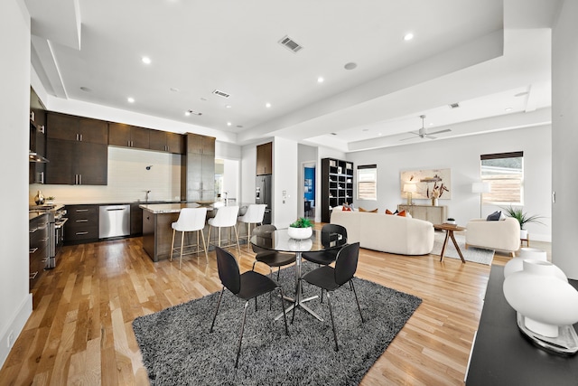 dining room featuring ceiling fan, sink, a tray ceiling, and light hardwood / wood-style floors