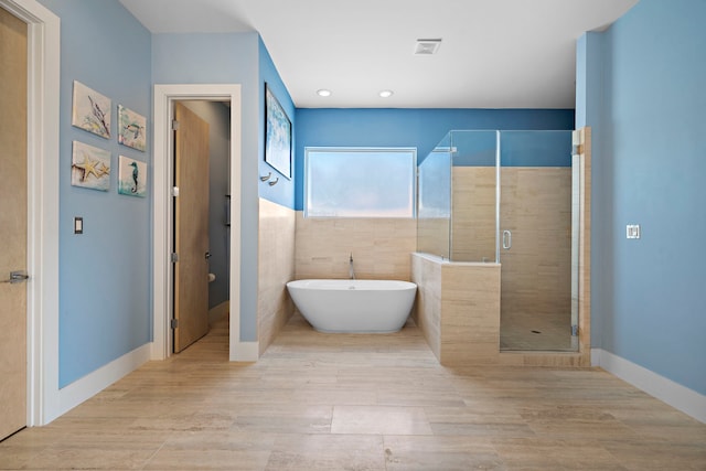 bathroom featuring plus walk in shower, wood-type flooring, and tile walls