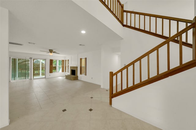 unfurnished living room with a brick fireplace, ceiling fan, and light tile patterned floors