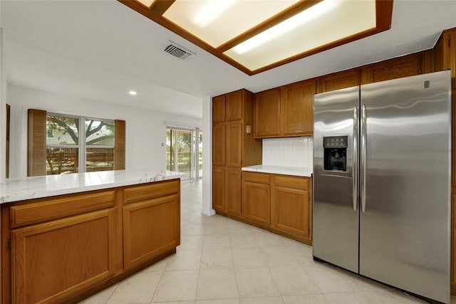 kitchen featuring light tile patterned flooring, stainless steel fridge, light stone counters, and tasteful backsplash