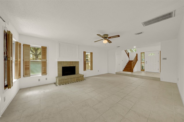 unfurnished living room featuring a textured ceiling, light tile patterned floors, ceiling fan, and a brick fireplace