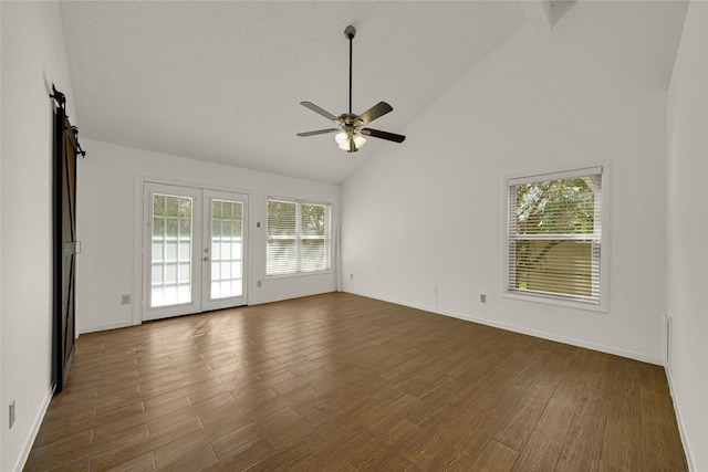 unfurnished room featuring ceiling fan, dark hardwood / wood-style floors, high vaulted ceiling, a barn door, and french doors