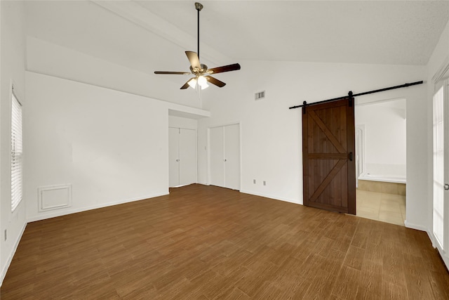 unfurnished room featuring lofted ceiling, a barn door, hardwood / wood-style flooring, and a healthy amount of sunlight