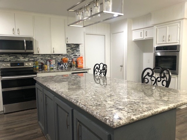 kitchen with stainless steel appliances, a kitchen island, dark hardwood / wood-style floors, light stone countertops, and white cabinets