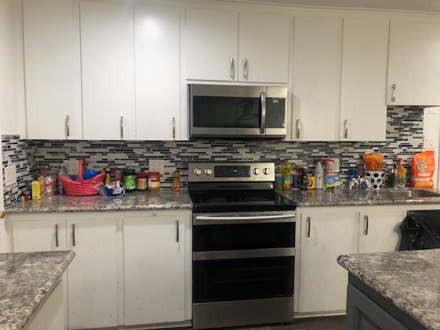 kitchen with white cabinets, dark stone counters, backsplash, and appliances with stainless steel finishes