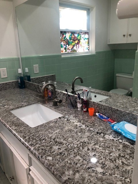 bathroom featuring toilet, vanity, and tile walls