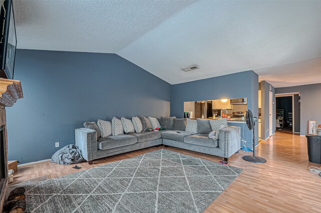 living room featuring wood-type flooring, a textured ceiling, and lofted ceiling