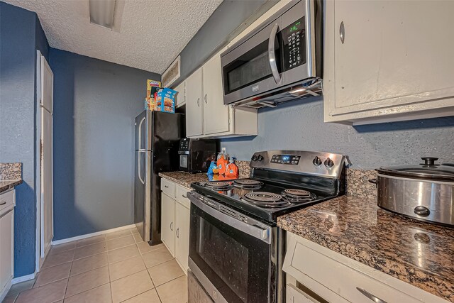 kitchen featuring stainless steel appliances, light tile patterned flooring, dark stone countertops, a textured ceiling, and white cabinets