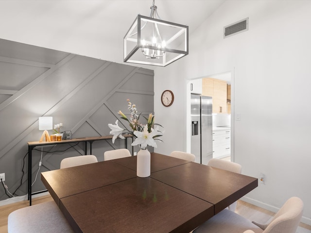 dining space with light hardwood / wood-style flooring, a notable chandelier, and vaulted ceiling