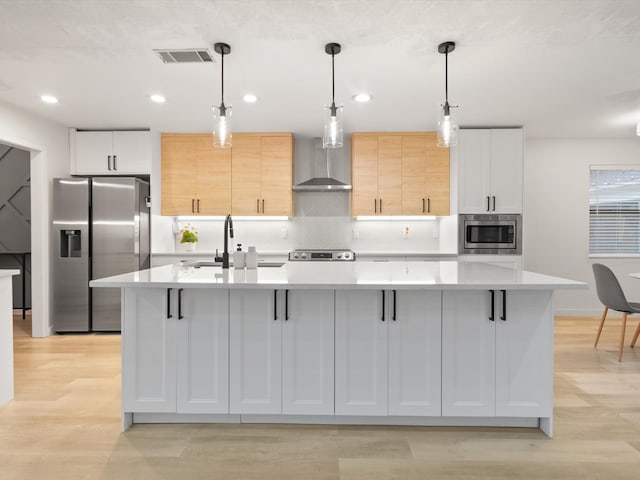 kitchen with white cabinets, wall chimney exhaust hood, a large island with sink, and decorative light fixtures