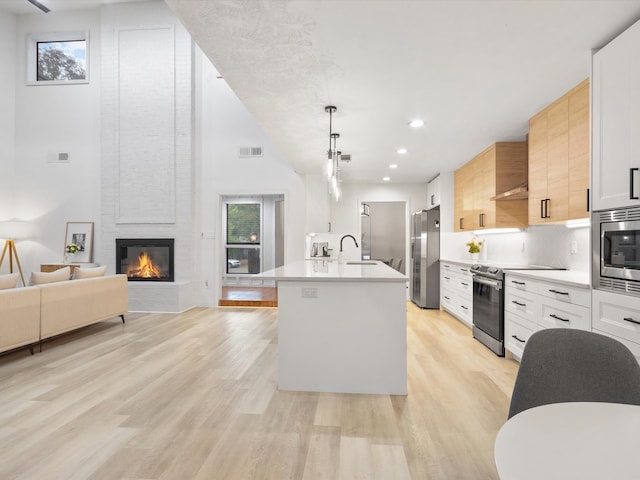 kitchen with pendant lighting, stainless steel appliances, an island with sink, and white cabinets