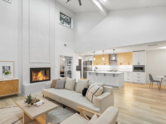 living room featuring high vaulted ceiling, light wood-type flooring, beam ceiling, and a fireplace