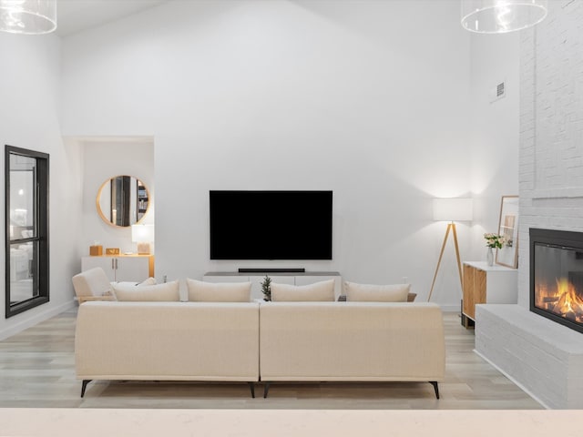 living room with a brick fireplace, a towering ceiling, and light wood-type flooring