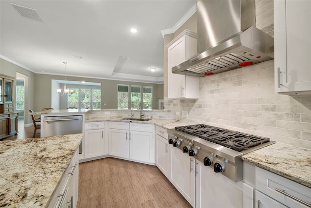 kitchen with appliances with stainless steel finishes, pendant lighting, sink, light hardwood / wood-style floors, and wall chimney exhaust hood