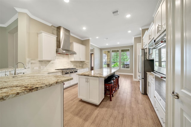 kitchen featuring light stone counters, light hardwood / wood-style flooring, a kitchen island, white cabinets, and wall chimney range hood