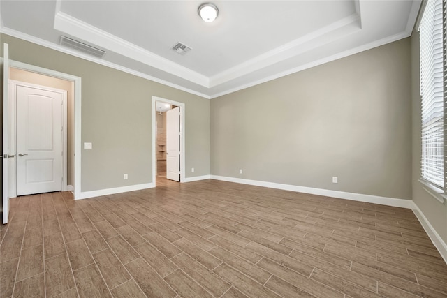 empty room featuring ornamental molding, light hardwood / wood-style flooring, and a raised ceiling