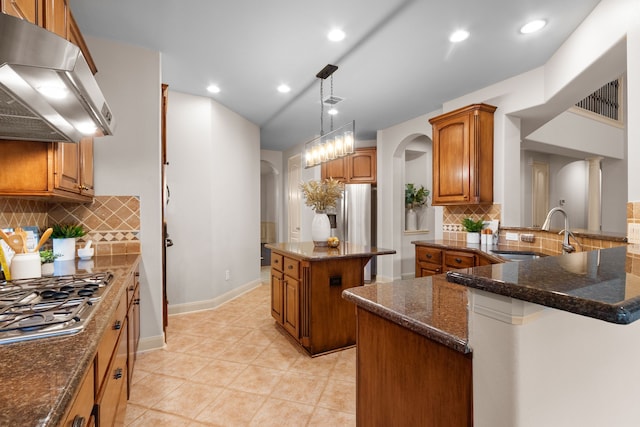 kitchen featuring stainless steel appliances, dark stone counters, extractor fan, sink, and a center island